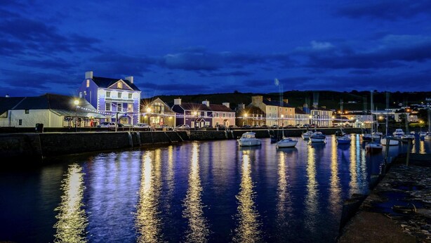 Un hotel frente al agua con un edificio destacado que dice "Harbourmaster Hotel", con una fachada grande e iluminada y un muelle con varios barcos.