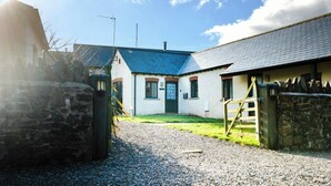 A gravel driveway leading to a building with a blue roof, a stone wall on the left, and a wooden gate on the right. - Toes Rock, Sandy Haven (Sandy Haven)