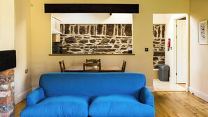 A living room with a blue sofa, a stone wall, a fireplace, and a dining area with chairs and a table. - Toes Rock, Sandy Haven (Sandy Haven)
