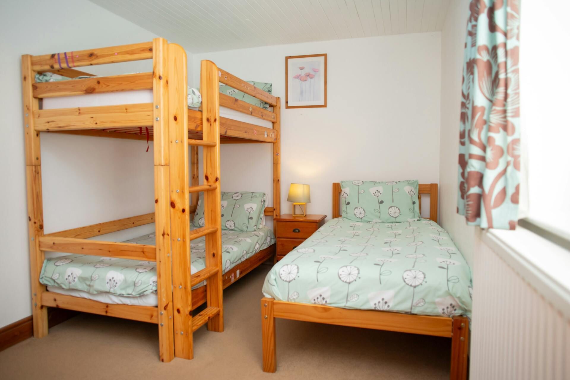 A room with two bunk beds, a bedside table with a lamp, and a framed picture on the wall.