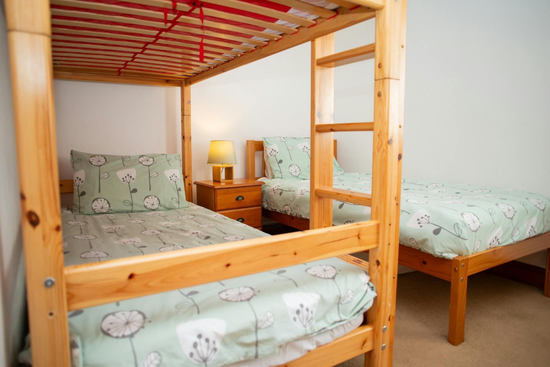 Ein Schlafraum mit Etagenbett aus Holz, einem Nachttisch mit Lampe und blumigem Bettbezug.