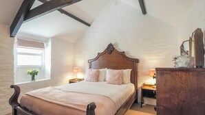 A bedroom with a wooden bed, a nightstand, a dresser, a window with a view, and exposed wooden beams on the ceiling. - The Coach House, Newcastle Emlyn (Newcastle Emlyn)