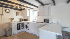 A compact kitchen with a washing machine, microwave, and a clock on the wall. - The Coach House, Newcastle Emlyn (Newcastle Emlyn)