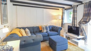 A living room with a sectional sofa, ottoman, TV stand, and a lamp. - The Coach House, Newcastle Emlyn (Newcastle Emlyn)