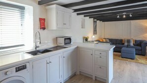 A compact kitchen with a washing machine, a microwave, and a sink. There is a fire blanket on the wall and a sofa in the adjacent living area. - The Coach House, Newcastle Emlyn (Newcastle Emlyn)