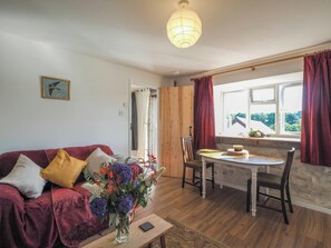 A cozy living room with a red sofa, a wooden dining table, and a vase of flowers. - Tanyfron, Llangrannog (Llwyndafydd)