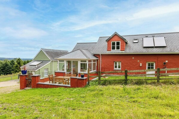 A red brick house with a covered porch, a fenced yard, and a clear sky.