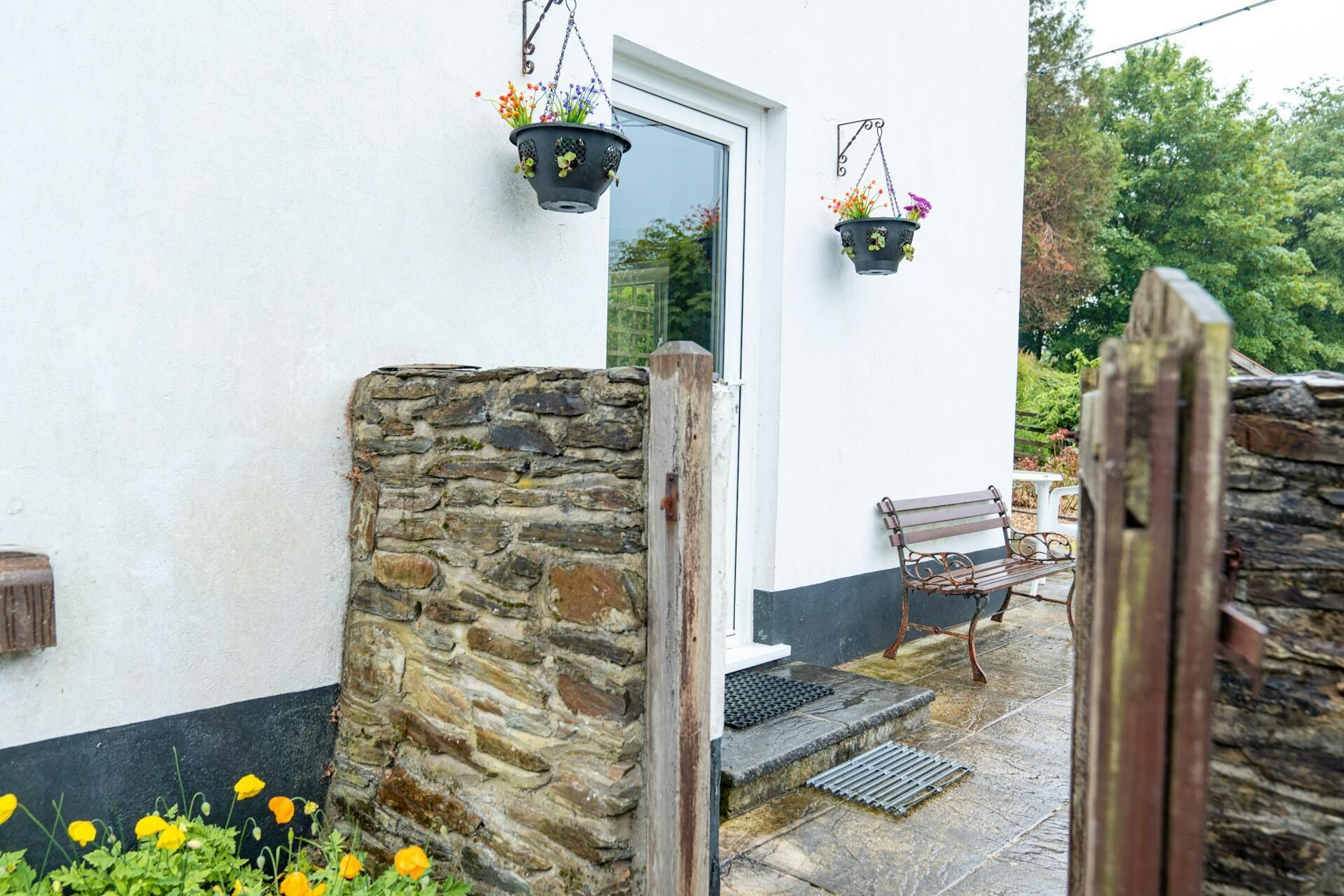 A stone wall, a wooden bench, and hanging flower pots at a building entrance.
