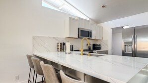 A modern kitchen with a marble countertop, stainless steel appliances, and bar stools. - Enchanting Escape with Playground near Disneyland (Anaheim)