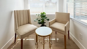 A corner room with two beige armchairs, a small round table, and a potted plant. - Enchanting Escape with Playground near Disneyland (Anaheim)