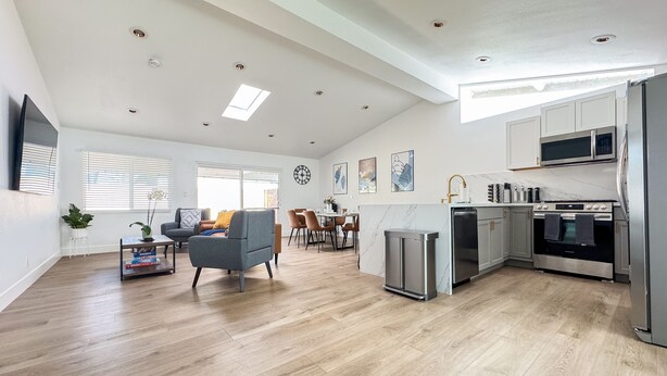 A spacious living room with a grey sofa, a dining area, and a kitchen with modern appliances. - Enchanting Escape with Playground near Disneyland (Anaheim)
