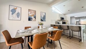 A modern dining area with a long table, brown chairs, and a kitchen in the background. - Enchanting Escape with Playground near Disneyland (Anaheim)