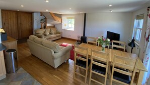 Uma sala de estar ampla com sofá, mesa de jantar com cadeiras, televisão e lareira.