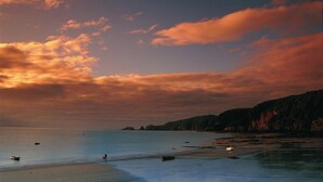 Un paysage côtier avec une plage, une mer calme et des collines à l’horizon.