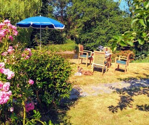A garden with a blue umbrella, wooden chairs, and a dog. - Penwaun, Newport - Three Bedroom Cottage, Sleeps 8 (Nevern)