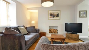 A cozy living room with a grey sofa, a wooden coffee table, a television, and a fireplace with wood logs.