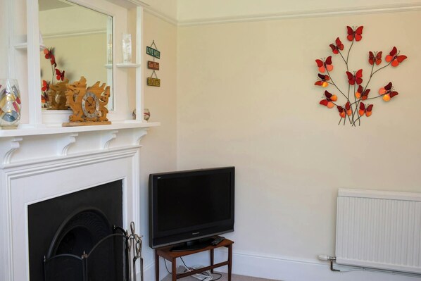 Un salon avec une cheminée, un téléviseur posé sur un meuble et une décoration murale composée de feuilles rouges et oranges.