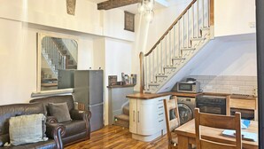 A cozy living room with a dark leather sofa, a wooden dining table, and a kitchen area with a microwave and stove. - Seymour, Johnston - Two Bedroom Cottage, Sleeps 4 (Johnston)