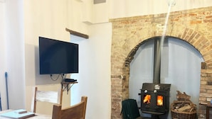 A cozy room with a wooden table, chairs, a television, and a stone fireplace with a wood-burning stove. - Seymour, Johnston - Two Bedroom Cottage, Sleeps 4 (Johnston)