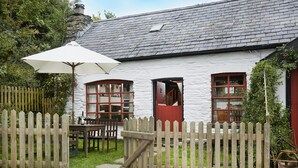 A white building with a stone chimney, wooden fence, and a table with chairs outside. - Y Beudy, Llangrannog (Llangrannog)
