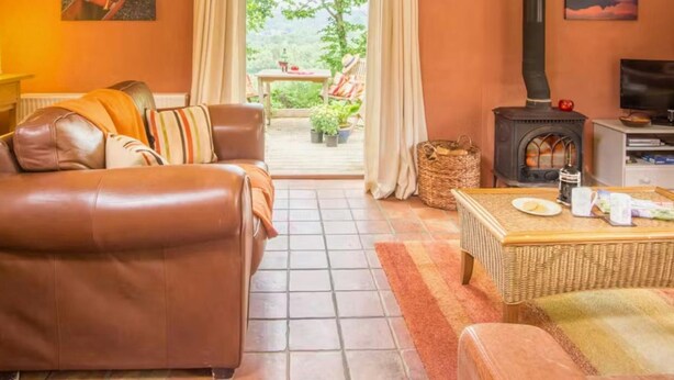 Ein gemütliches Wohnzimmer mit Ledersofa, Korbstuhl Tisch und Kaminofen.