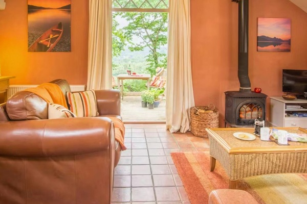 Spacious living area with sofa, wicker coffee table, TV and log burner; external door leading to outside seating area