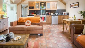 Ein gemütliches Wohnzimmer mit einem braunen Ledersofa, einem Couchtisch mit Buch und Teekanne, sowie einem Essbereich mit Holztisch und Stühlen.