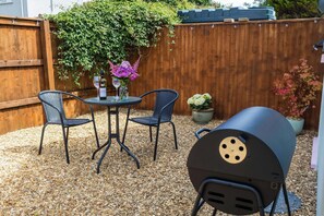 Een terras met een ronde tafel, vier stoelen, een barbecue en planten in potten.