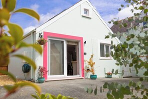 A single-story building with a pink door and windows, a small attached garage, and potted plants.