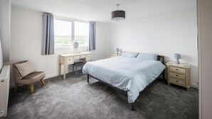 Une chambre à coucher avec un lit, des tables de chevet, un bureau, une chaise et une fenêtre avec des rideaux.