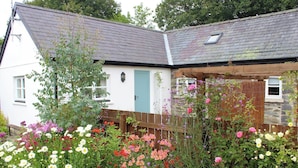A white building with a grey roof, a wooden fence, and a variety of flowering plants.