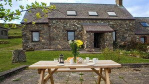 A stone house with a garden table set for a meal, featuring a vase with flowers, a teapot, and cups.