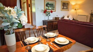 A dining table set with plates, glasses, and cutlery, a wooden cabinet, a sofa, and two framed artworks on the wall.