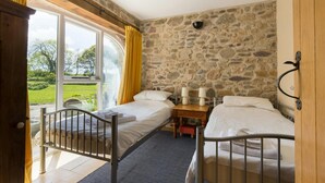 Un dormitorio con dos camas, una pared de piedra, una puerta de madera y vistas a un paisaje verde.