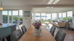A spacious dining area with a wooden table, chairs, and a vase of flowers. - Pentir, Gwbert - Four Bedroom Cottage, Sleeps 7 (Gwbert)