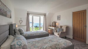A bedroom with two beds, a desk, a chair, a wooden door, and a view of the sea. - Pentir, Gwbert - Four Bedroom Cottage, Sleeps 7 (Gwbert)
