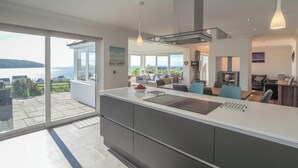 A modern kitchen with a large island, a dining area with a view, and a living room with a fireplace. - Pentir, Gwbert - Four Bedroom Cottage, Sleeps 7 (Gwbert)