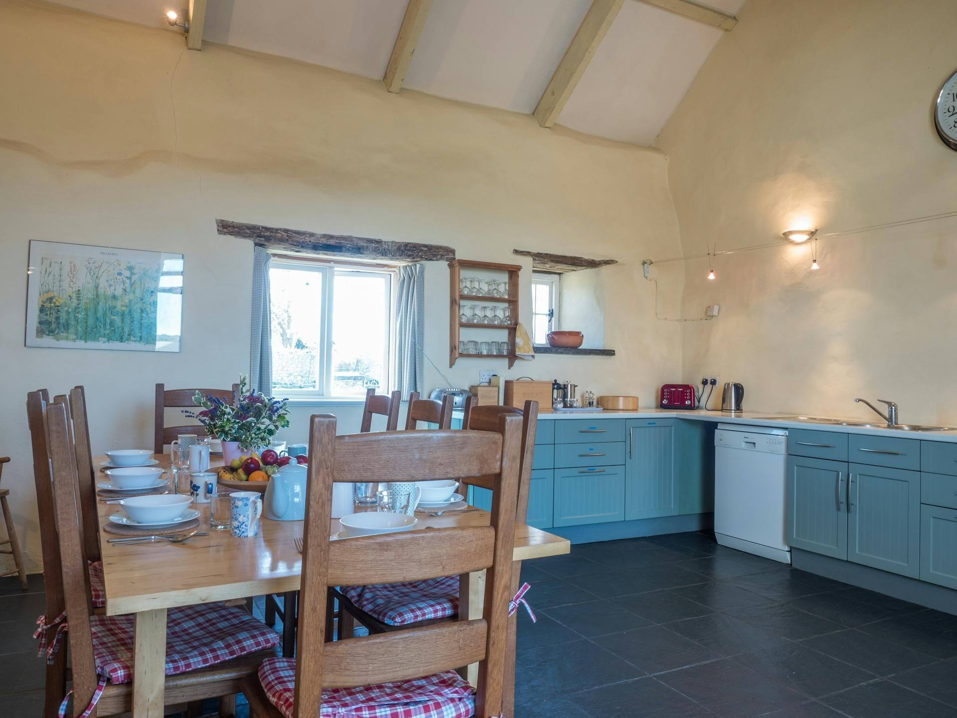 A dining area with a wooden table set for four, a kitchen with blue cabinets, and a window with curtains.