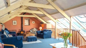 A cozy attic room with a sloped ceiling, blue sofas, a wooden table, and a view through a skylight.