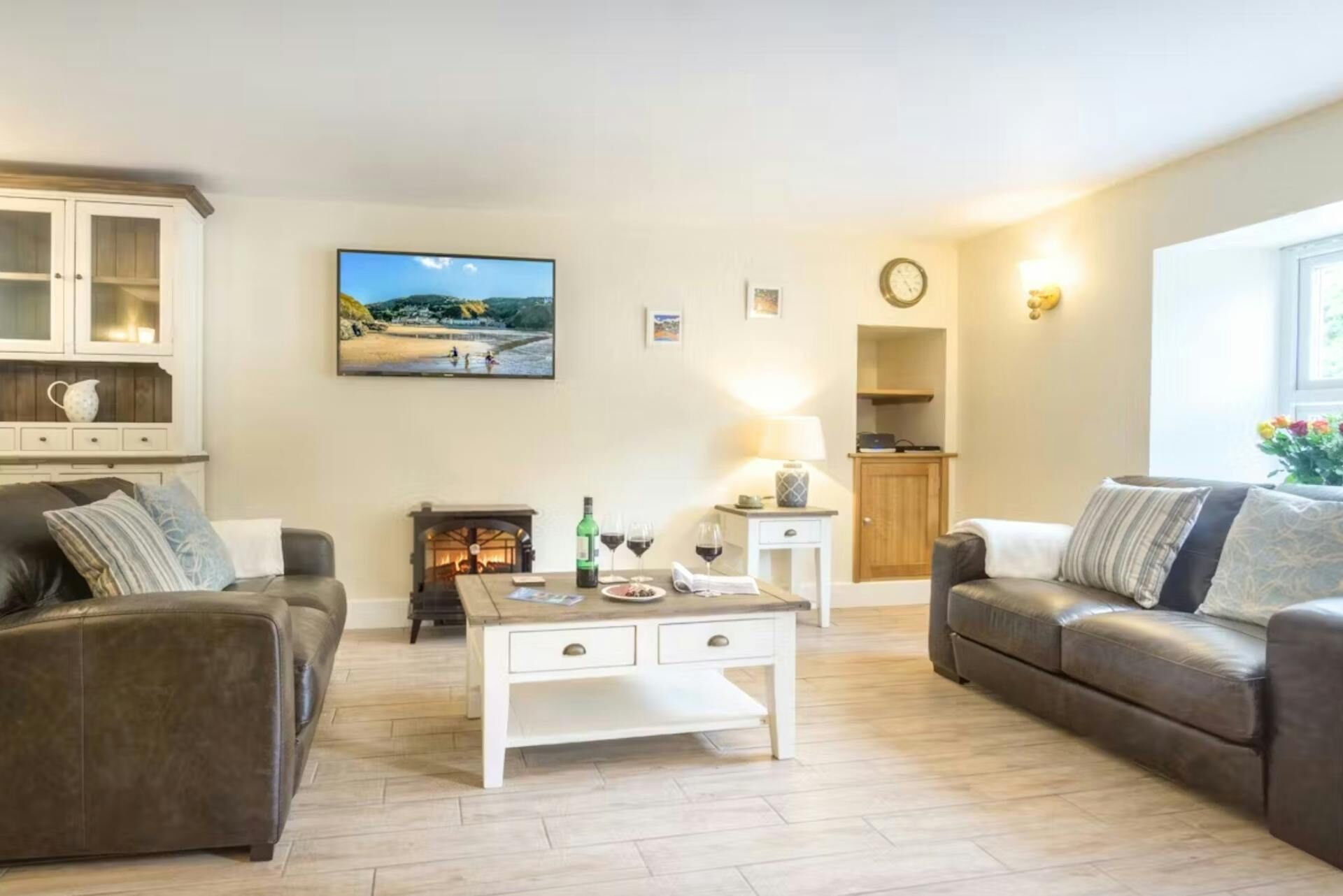 A living room with two sofas, a coffee table, a fireplace, a television, and a clock on the wall.