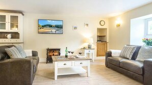 Ein Wohnzimmer mit zwei Sofas, einem Couchtisch, einem Kamin, einem Fernseher und einer Wanduhr.