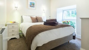 Ein Schlafzimmer mit Bett, Nachttischen, Heizkörper, Fenster mit Blick und einem gerahmten Bild an der Wand.