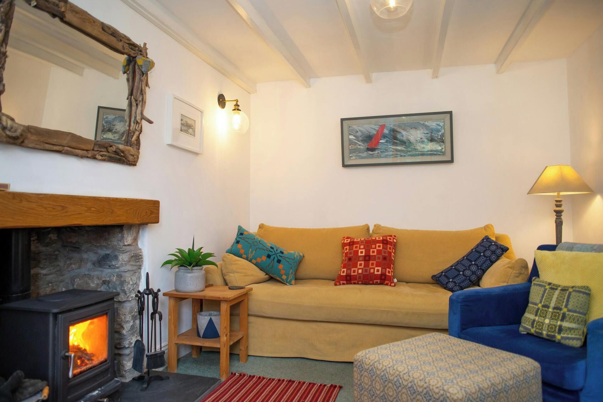 A cozy living room with a stone fireplace, a sofa, a blue armchair, and a painting on the wall.