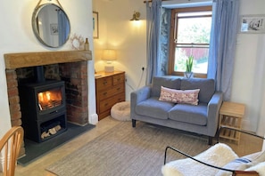 A cozy living room with a fireplace, a sofa, a wooden dresser, and a window with curtains.