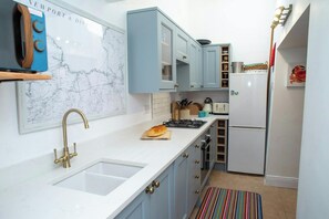 A kitchen with a white sink, blue cabinets, a map on the wall, a stove, and a refrigerator.