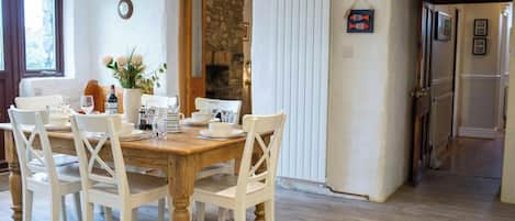 Un coin repas avec une table en bois et des chaises blanches, un mur en pierre et un radiateur blanc.