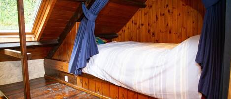 A cozy attic bedroom with a wooden ceiling, a bed with white bedding, and blue curtains.