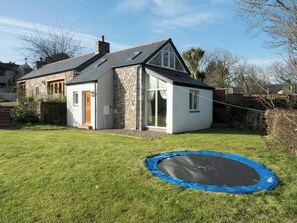 Ein Haus mit Steinaußenwand, schwarzem Dach und blauem Trampolin im Garten.