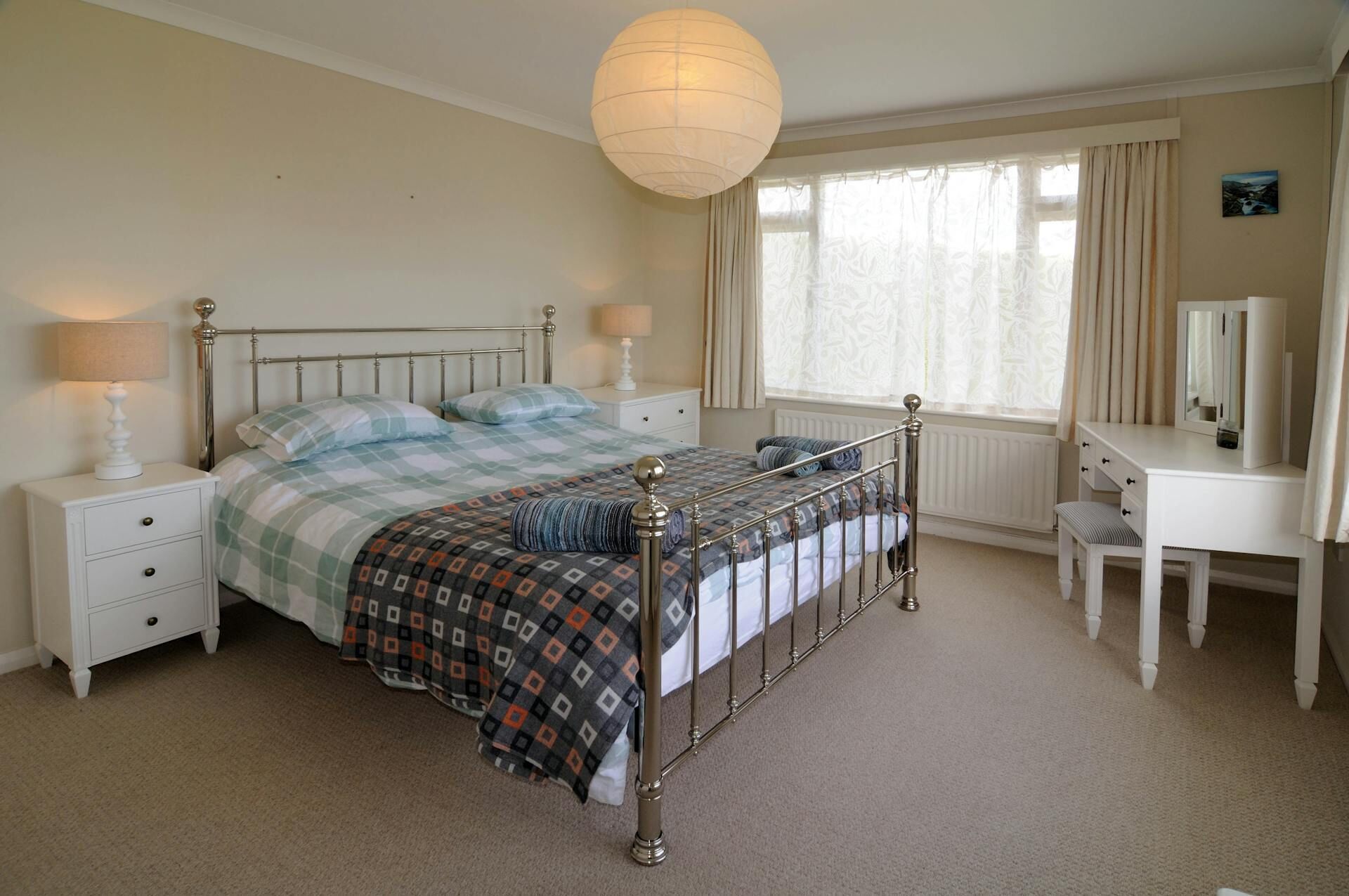 Une chambre à coucher comprenant un lit, des tables de chevet, une commode, un miroir et un luminaire suspendu.