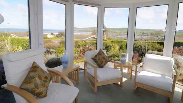 Un solárium con mobiliario blanco y ventanas amplias que dan a un paisaje pintoresco.